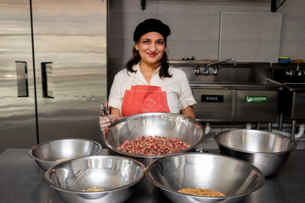Divya wearing red apron and black cap at a kitchen working with organic rose pitta tea