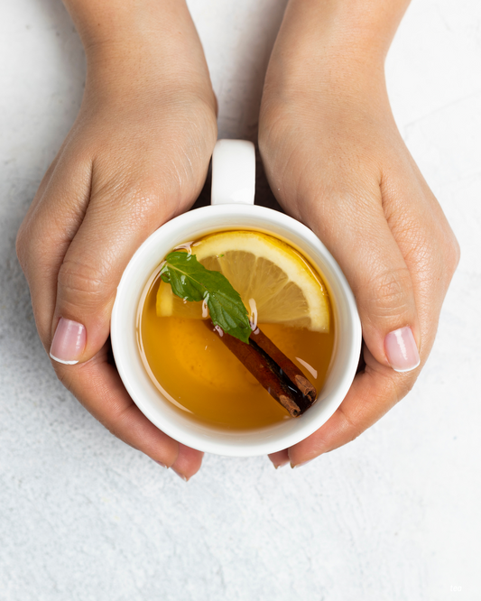 a cup of herbal tea with cinnamon mint and lemon held in two hands on a white background