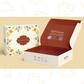 A wellness gift box with floral patterns on the lid and a red interior. The box is branded with 'AyurSome Wellness'. Customers can add any 3 organic herbal teas and ancient grain cookies to the box. 