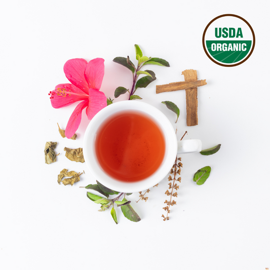Brewed Gymnema aka Gurmar tea in a white cup. Outside the cup are Organic gymnema leaf tea, tulsi aka holy basil, hibiscus and cinnamon. On the right top corder is the USDA Organic logo to indicate that the herbal tea is organic. 