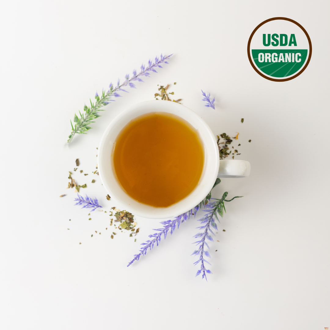 A white cup of lavender and lemon balm tea, which is the best tea for sleep. Outside the cup are lavender, the best her for anxiety and soothing lemon balm leaf. USDA organic logo is on the right top corner