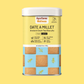 A cylindrical metal tin of AyurSome Wellness Date A Millet cookies, featuring a yellow upper label, a light blue lower section with printed millet cookies illustrations, and a white lid. The flavor is Lemon and the cookies have no refined sugar, are made with whole grains and are plant based.