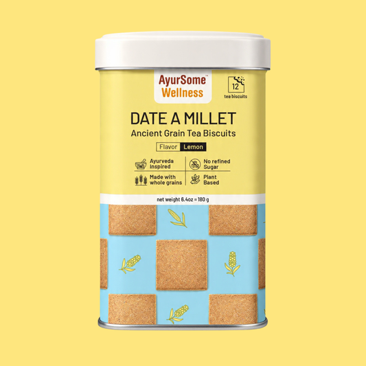 A cylindrical metal tin of AyurSome Wellness Date A Millet cookies, featuring a yellow upper label, a light blue lower section with printed millet cookies illustrations, and a white lid. The flavor is Lemon and the cookies have no refined sugar, are made with whole grains and are plant based.