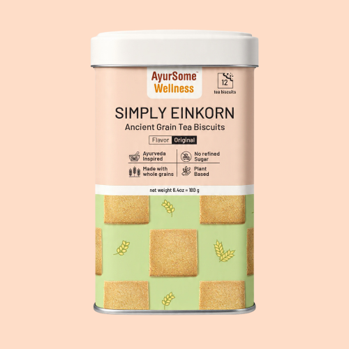 A square cookie tin of Simply Einkorn cookies by AyurSome Wellness. The tin is of wheat and cardamom color. The background is of whole wheat color as well. The cookie tins has pictures of the vegan einkorn cookies that are packed in the tin. 